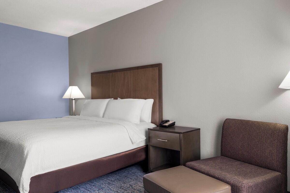 A hotel room with a bed, bedside table, lamp, and a chair.