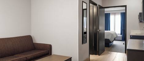 A hotel room with a sofa, a small table, a door leading to a bedroom, and a bathroom.