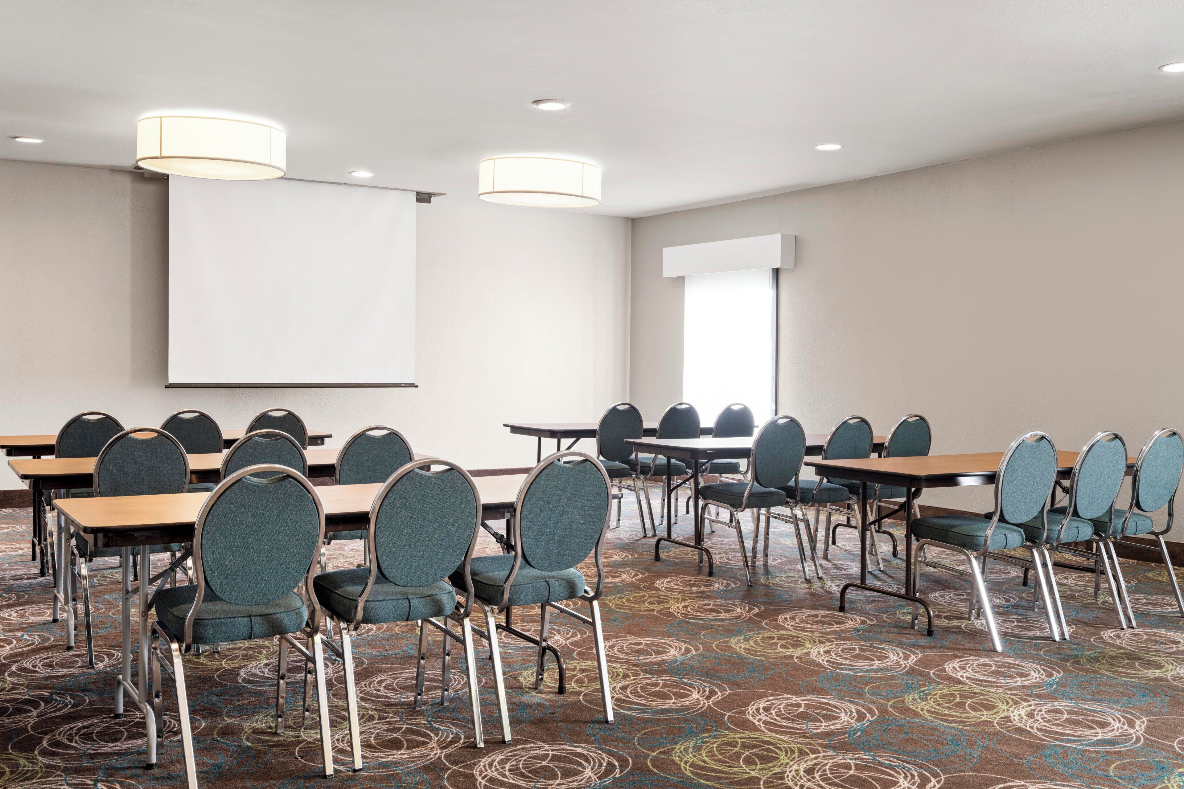 A conference room with tables and chairs, a projector screen, and a large window.