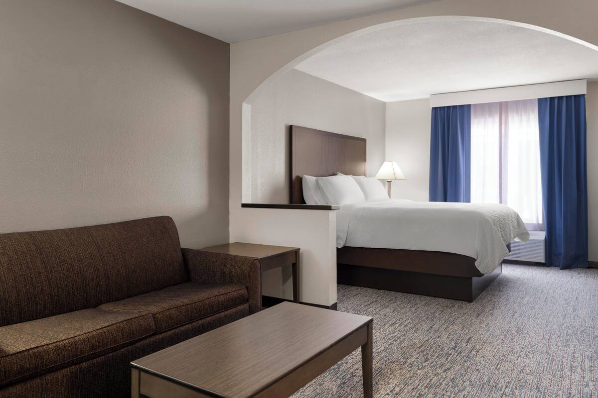 A hotel room with a sofa, a bed, a nightstand, and a lamp.