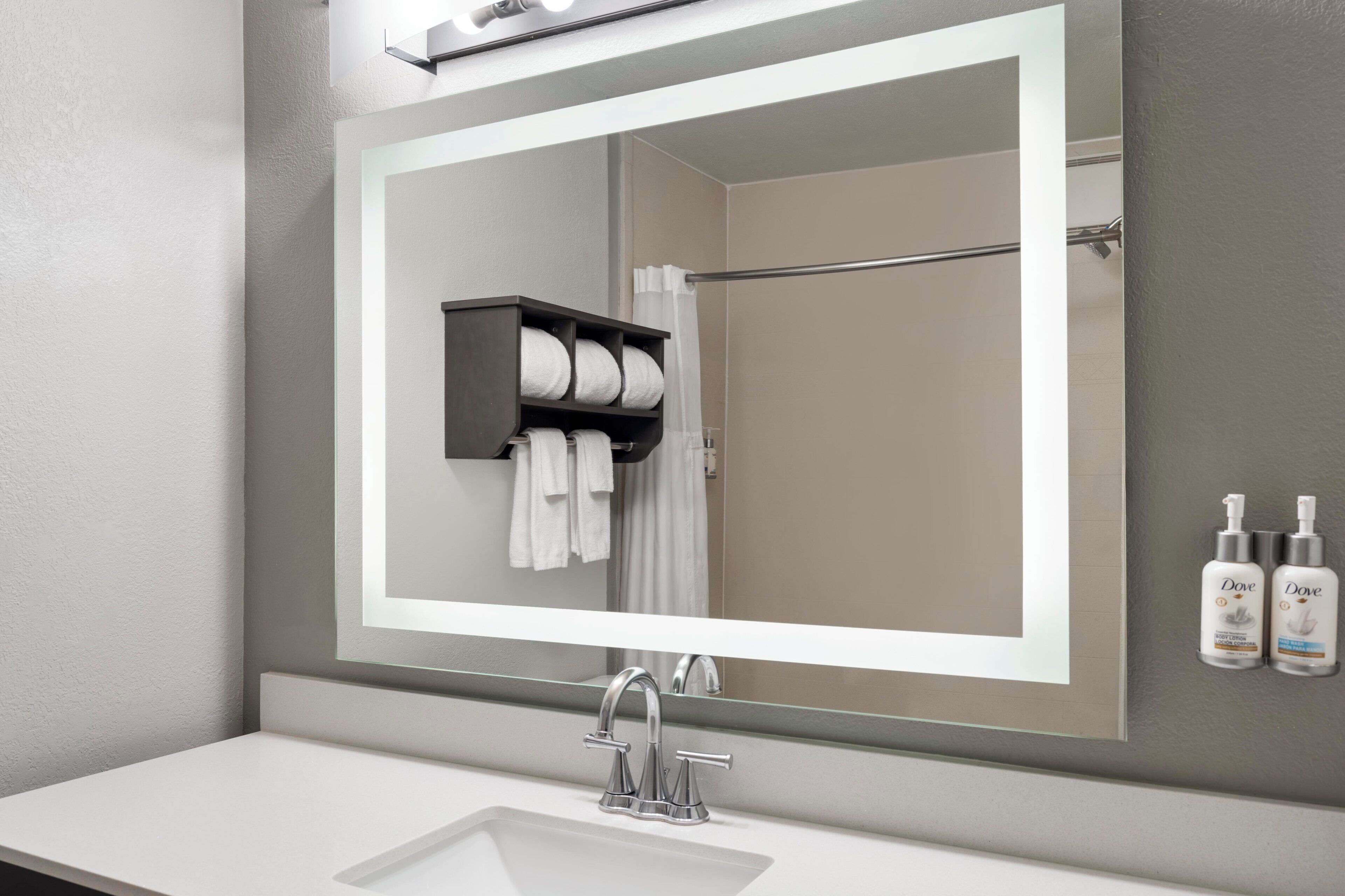 Une salle de bain avec un grand miroir, un lavabo blanc, un porte-serviettes et des produits de toilette de la marque Dove.