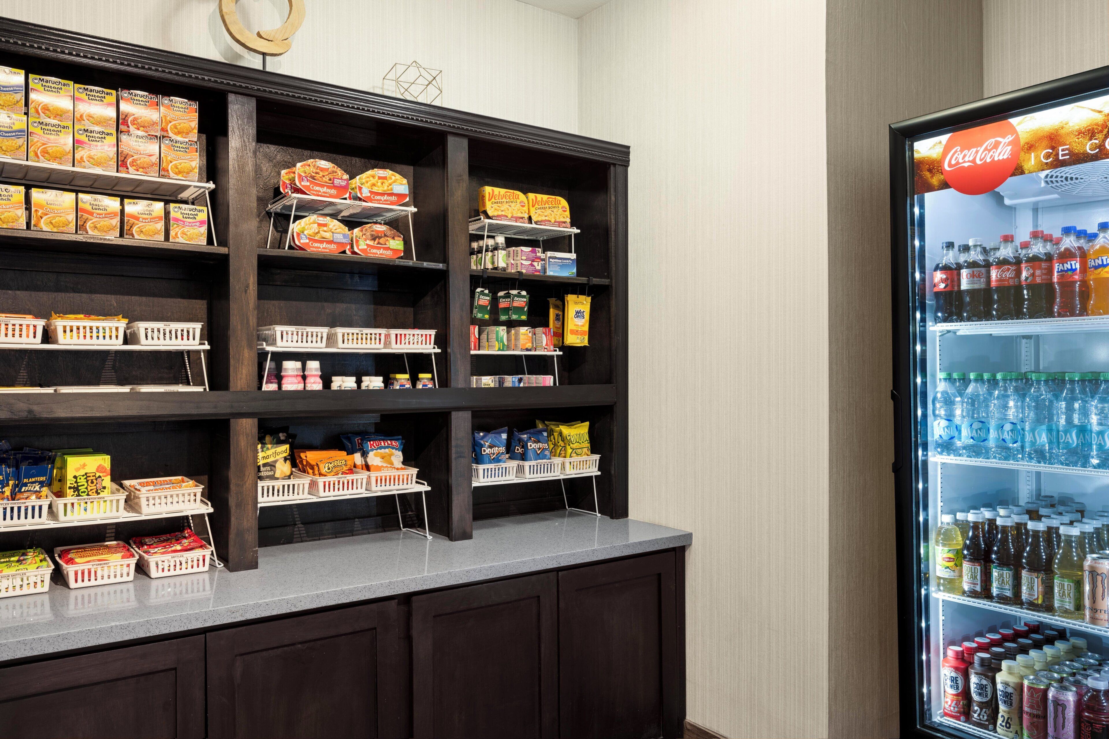 Un espace de libre-service où l’on peut se servir des boissons, avec un réfrigérateur à Coca-Cola et une variété de collations et de condiments disposés sur des étagères.