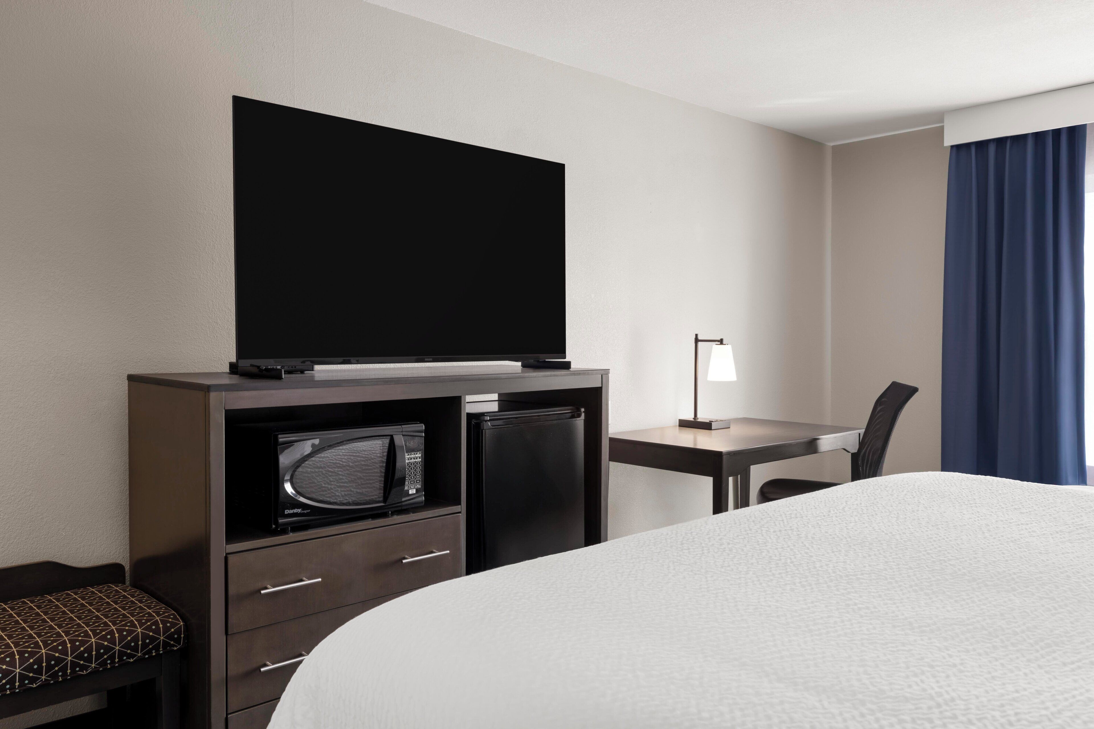 A hotel room with a bed, a television, a microwave, a refrigerator, a desk, and a chair.