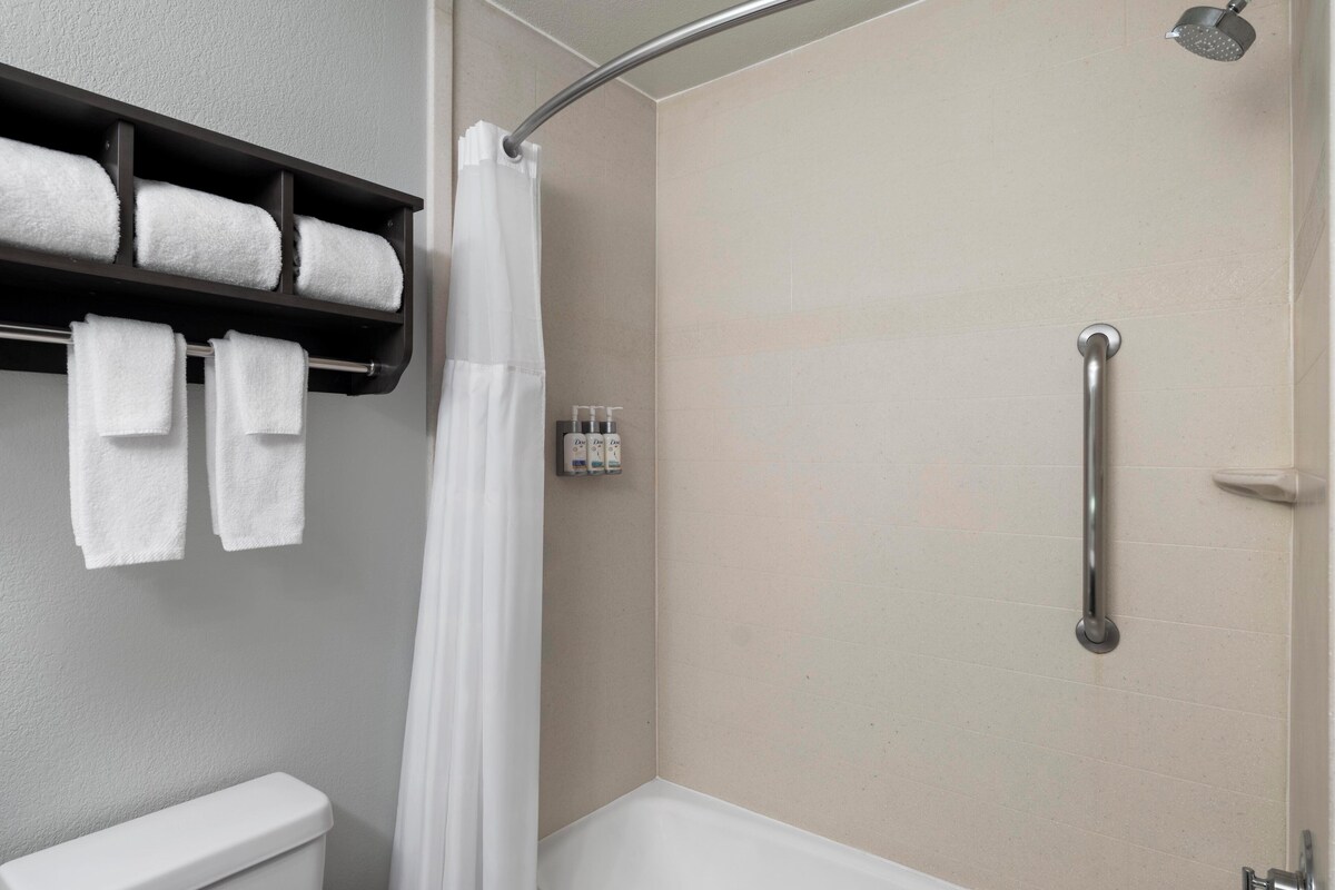 A shower with a handheld showerhead, a grab bar, and a towel rack with towels.