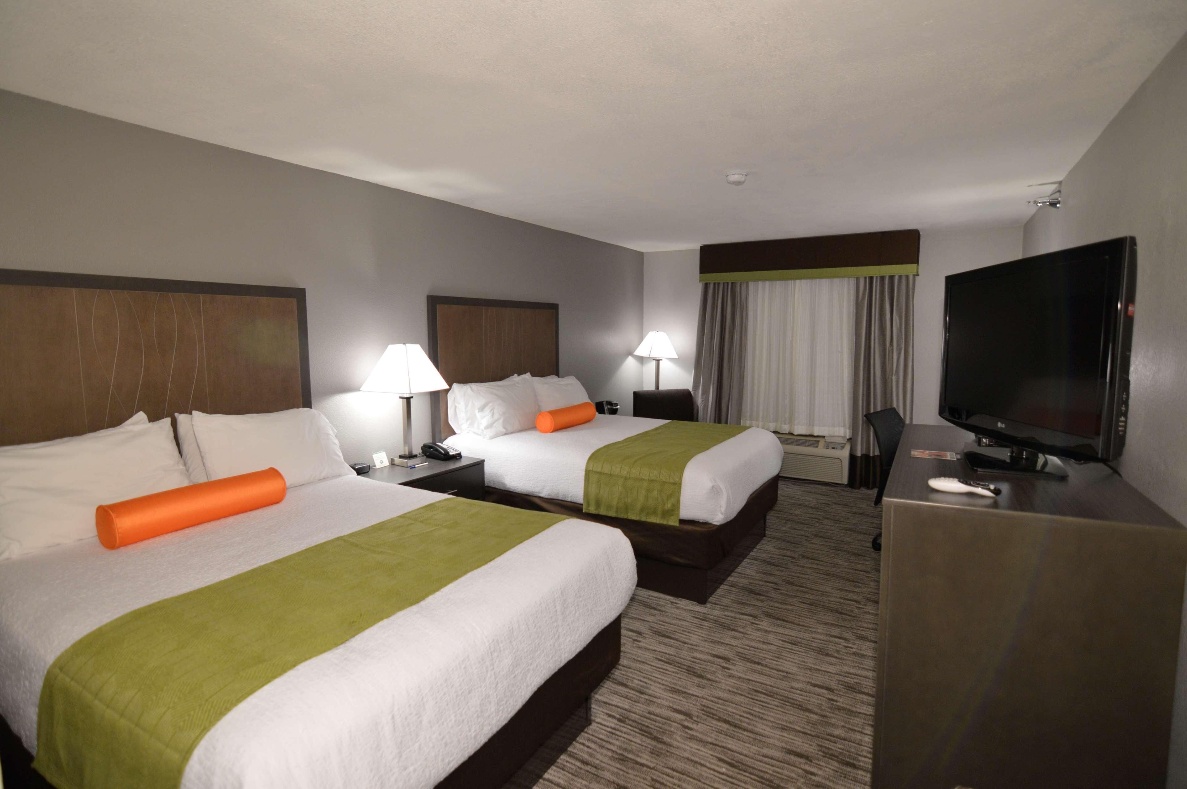 A hotel room with two beds, a desk, a television, and a window with curtains.