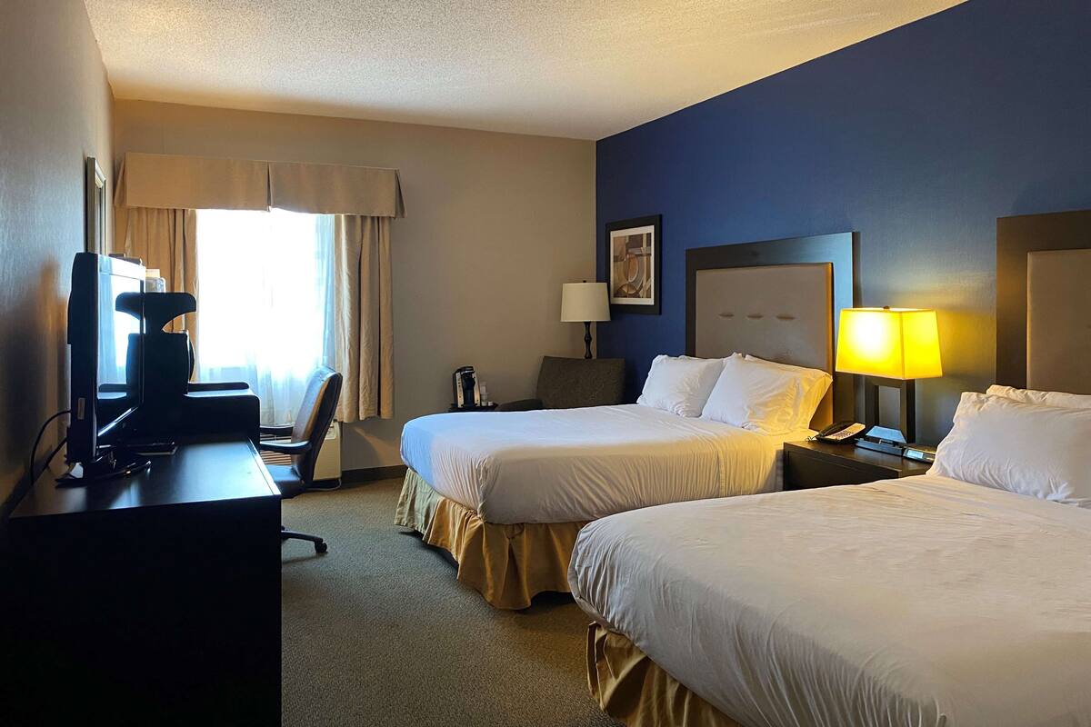 Habitación de hotel con dos camas, un escritorio con computadora, una silla, una lámpara y una mesita de noche con teléfono.