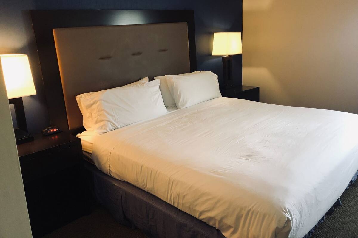 A hotel room with a large bed, two bedside tables with lamps, and a dark headboard.