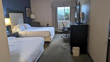 A hotel room with two beds, a desk, a chair, a TV, and a window with curtains.