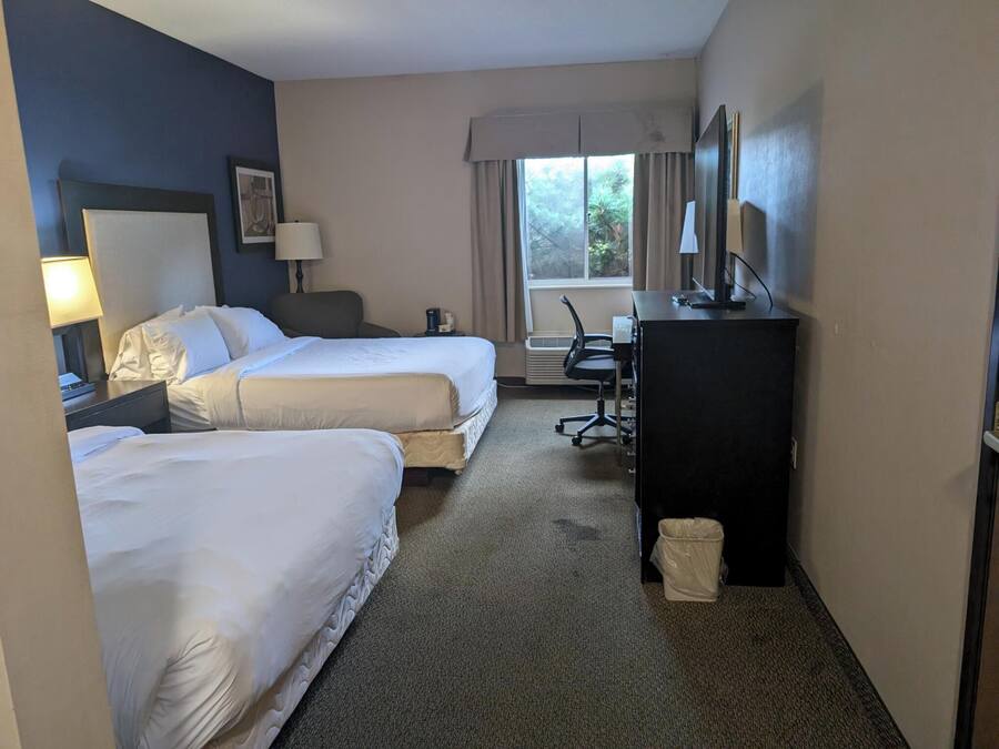 Une chambre d’hôtel avec deux lits, un bureau, une chaise, une télévision et une fenêtre avec des rideaux.