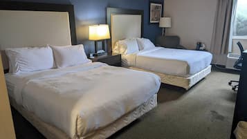 Camera d'albergo con due letti, una scrivania, una sedia, una lampada e una finestra.
