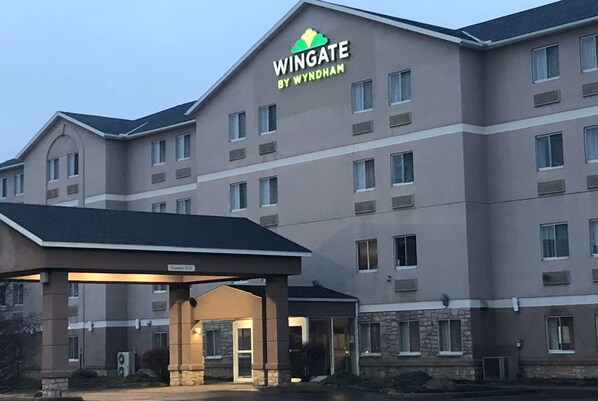 Experience the sleek entrance and modern design of The Wingate hotel, featuring a covered parking area and multiple floors with evenly spaced windows.