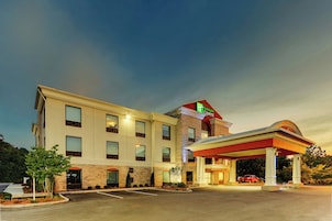 Un hotel Holiday Inn Express con una gasolinera adosada, que cuenta con un estacionamiento y una camioneta roja.