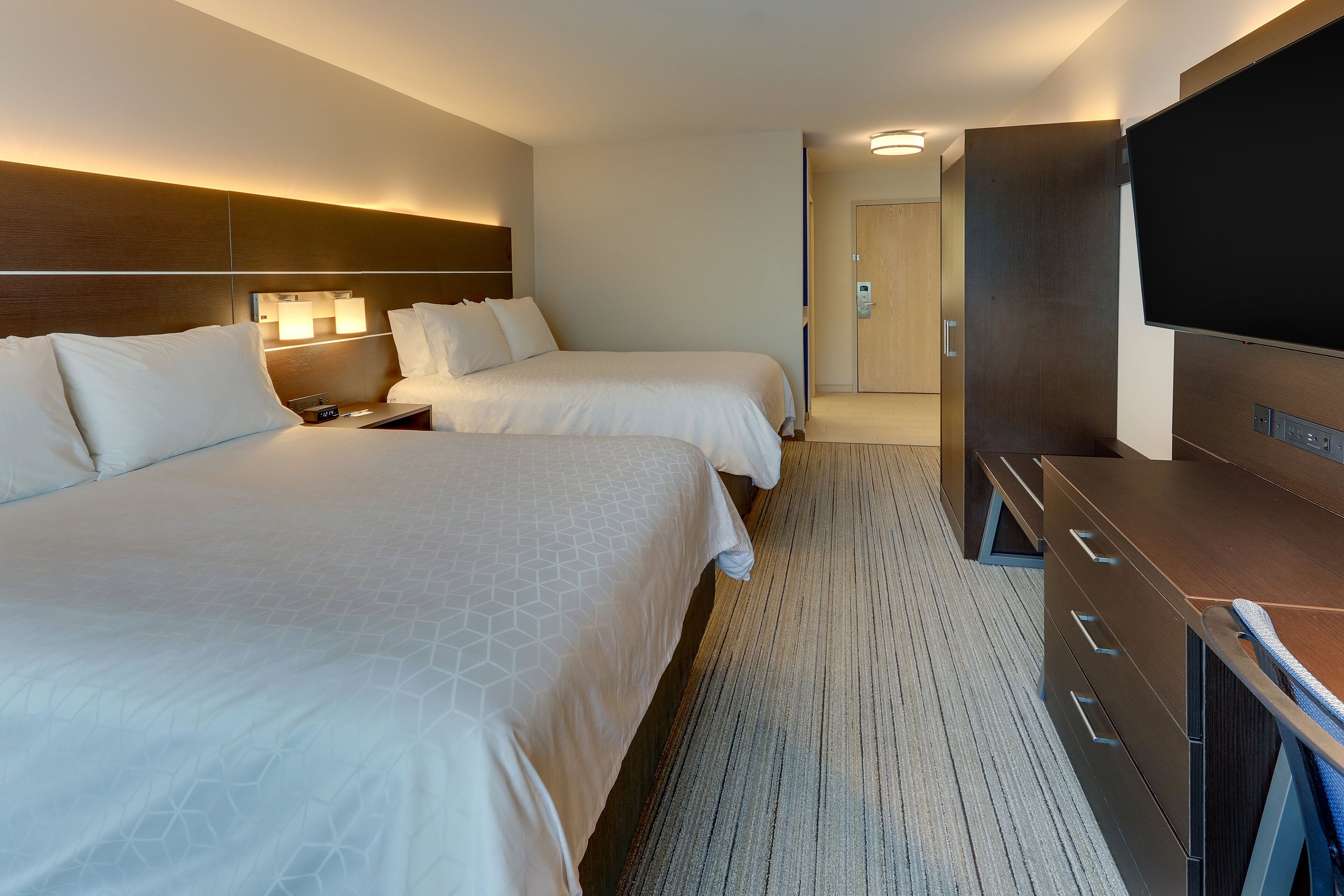 A hotel room with two beds, a flat-screen TV, a desk, and a walk-in closet.