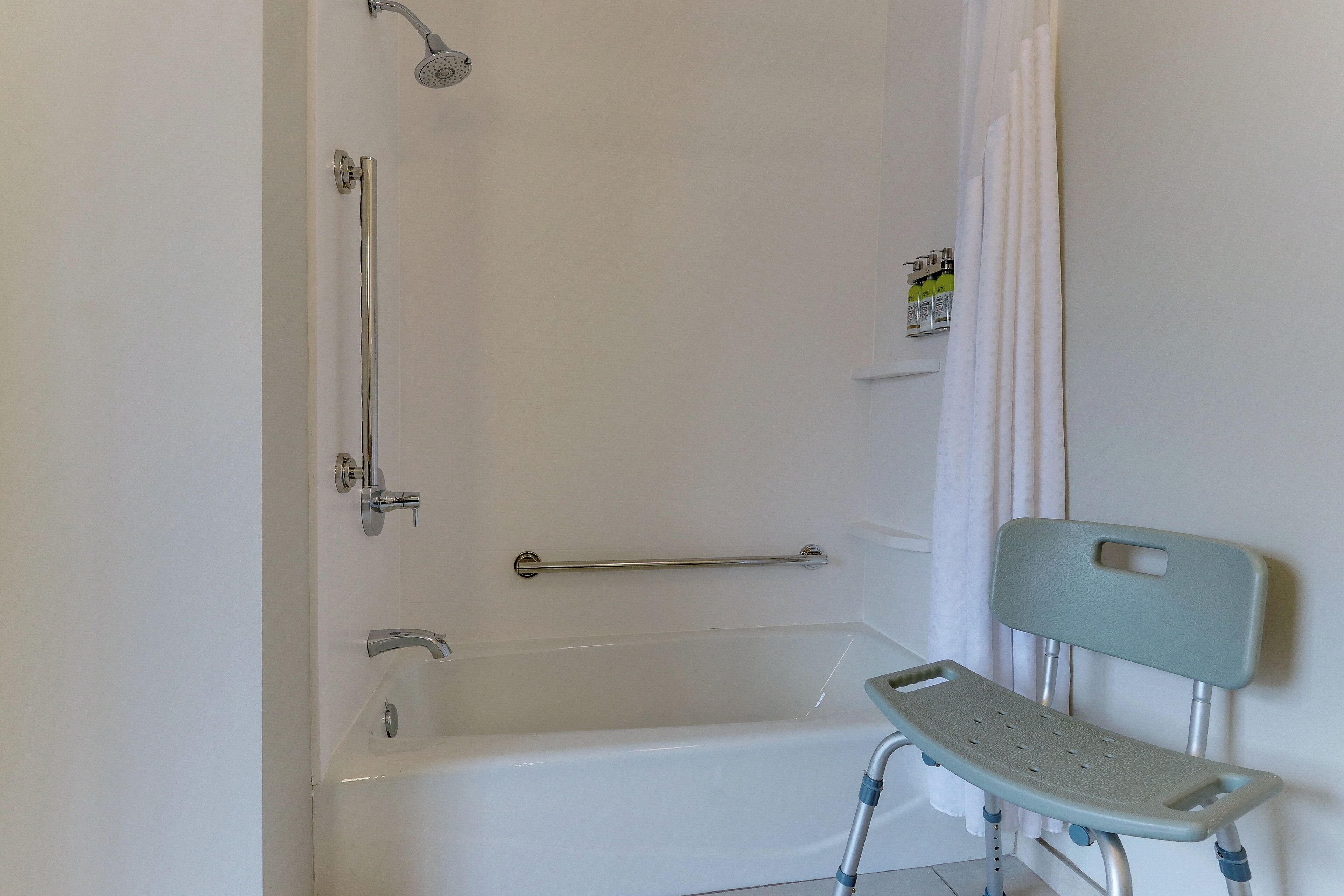 A bathroom with a bathtub, a shower, a handrail, and a wheelchair-accessible bench.