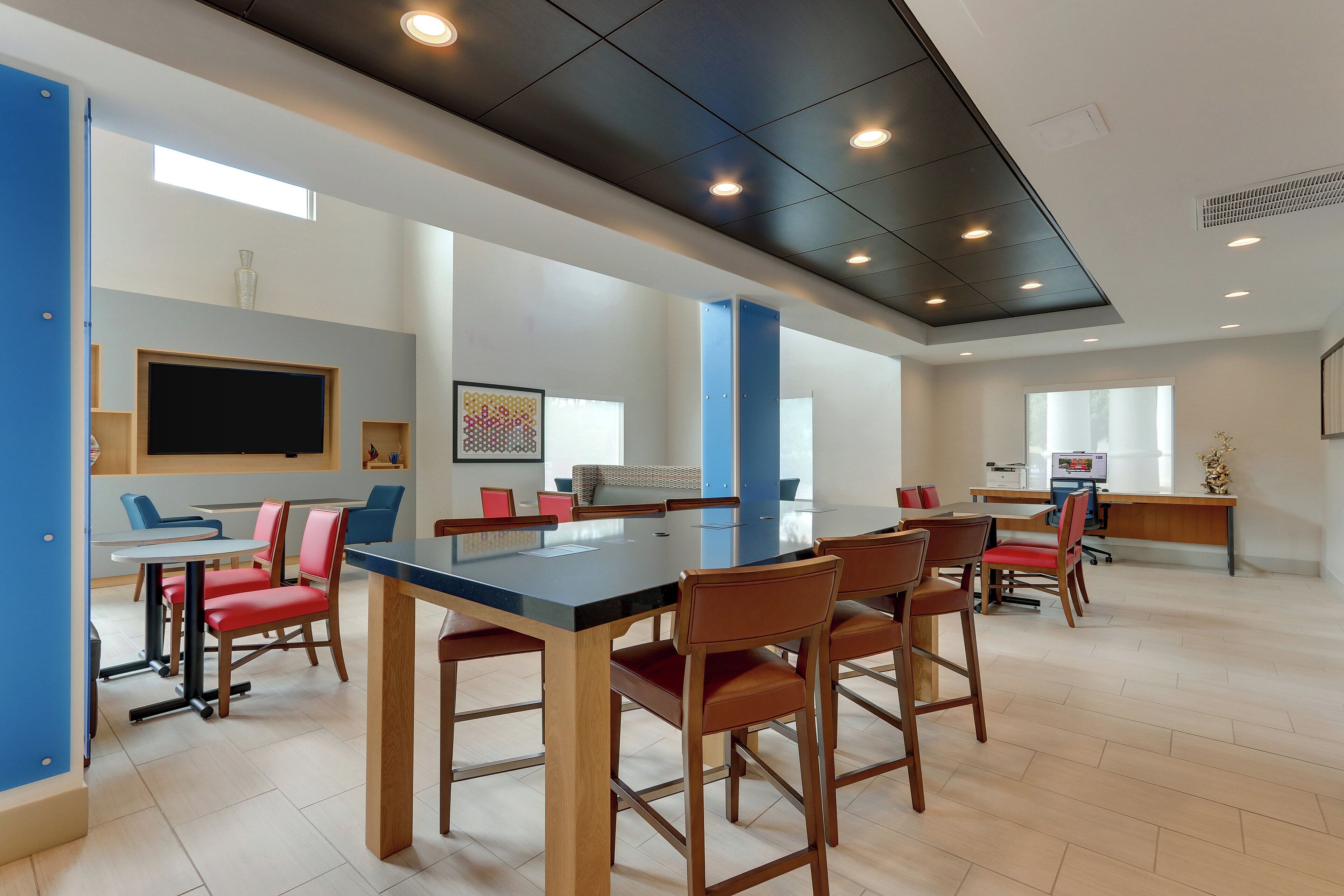 A spacious room with a long table, several chairs, and a television on the wall.