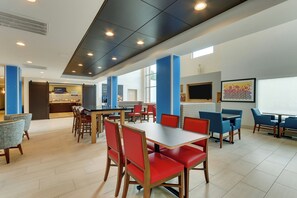 A modern dining area with red and blue seating, a breakfast bar, and a large window providing natural light. - Holiday Inn Express & Suites Corbin by IHG (Corbin)