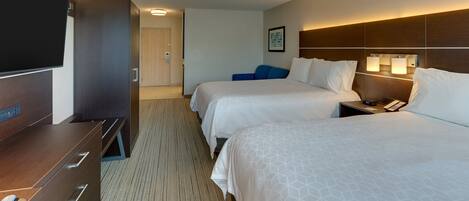 A hotel room with two beds, a TV, a desk, and a minibar.