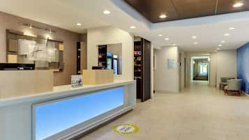 A hotel reception area with a modern design, a reception desk, a digital display, and a corridor leading to other areas.