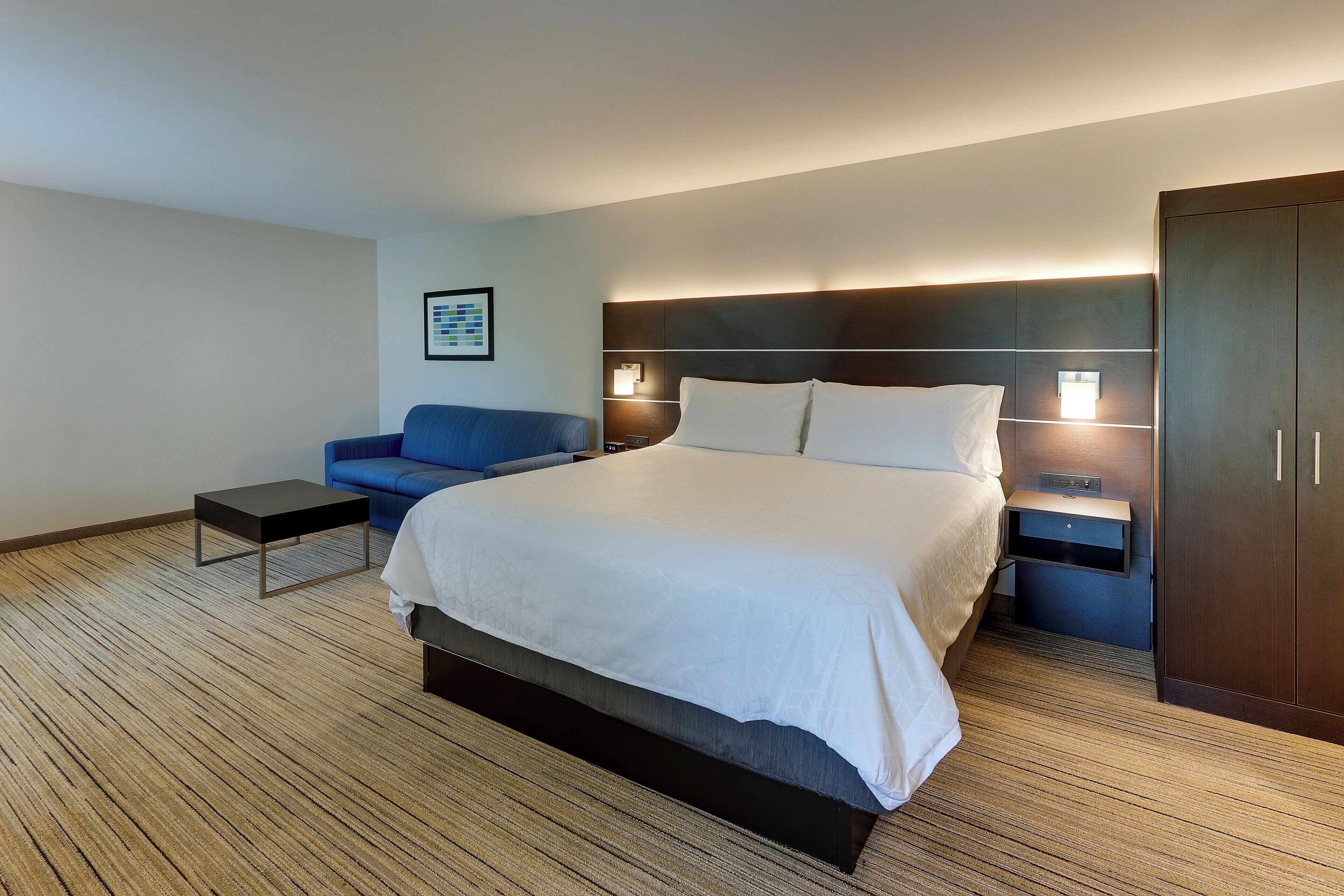 A hotel room with a large bed, a blue sofa, a small table, and a wardrobe.