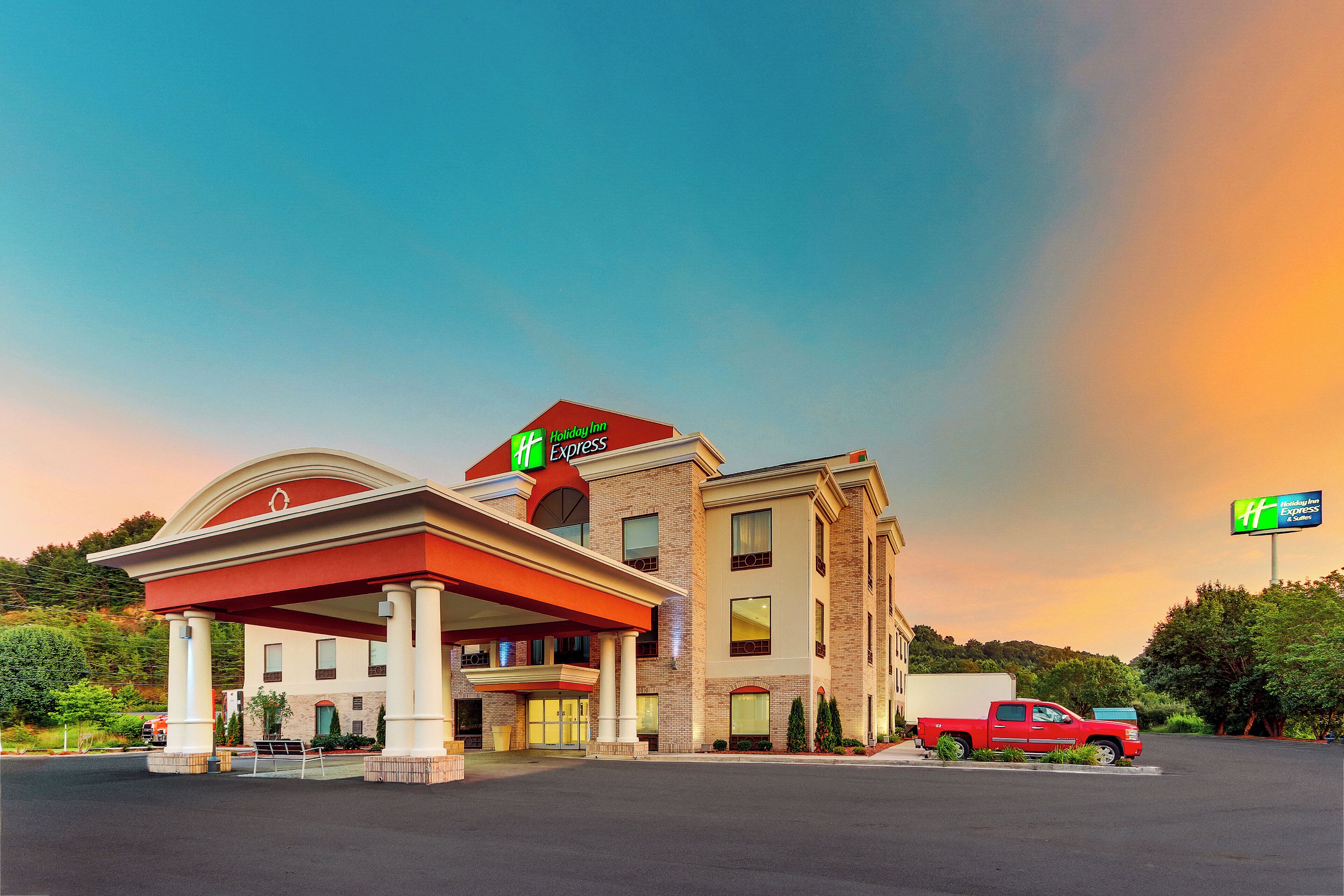 Edifício Holiday Inn Express com toldo de posto de gasolina, uma caminhonete vermelha estacionada na frente e céu azul.