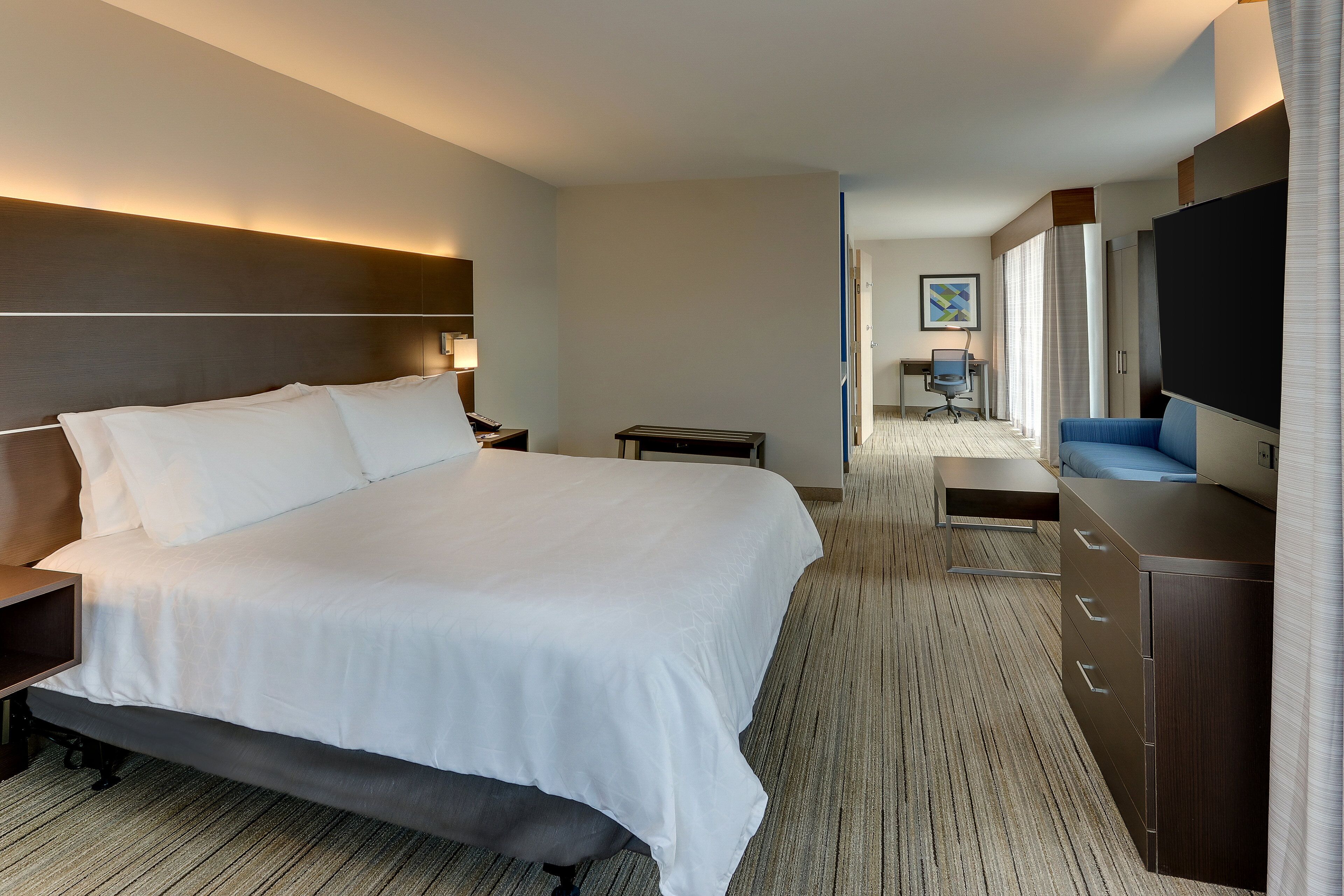 Una habitación de hotel con una cama grande, un escritorio, una silla, un televisor y un armario.