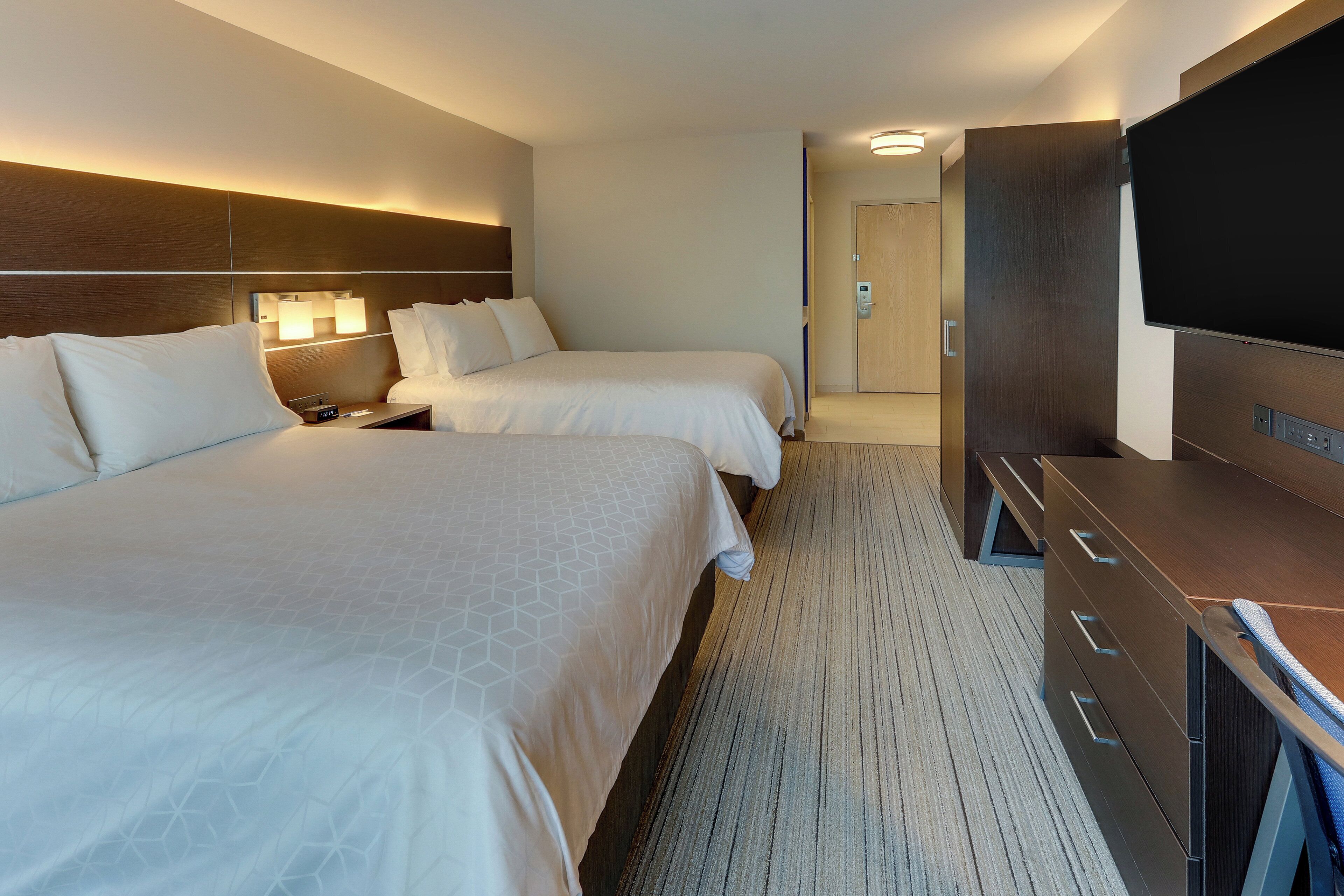 Ein Hotelzimmer mit zwei Betten, einem Flachbildfernseher, einem Schreibtisch und einem Kleiderschrank.
