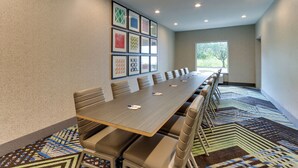 A conference room with a long table, multiple chairs, framed artwork on the wall, and a view through the window.