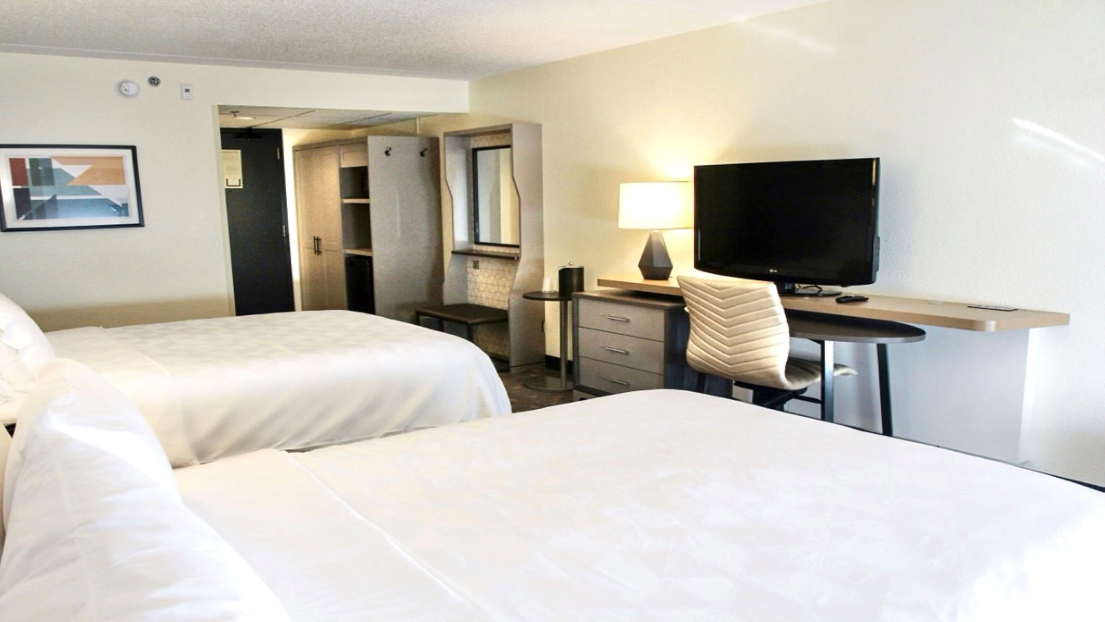 Une chambre d’hôtel avec deux lits, un bureau avec une télévision, une chaise, une lampe et une armoire.