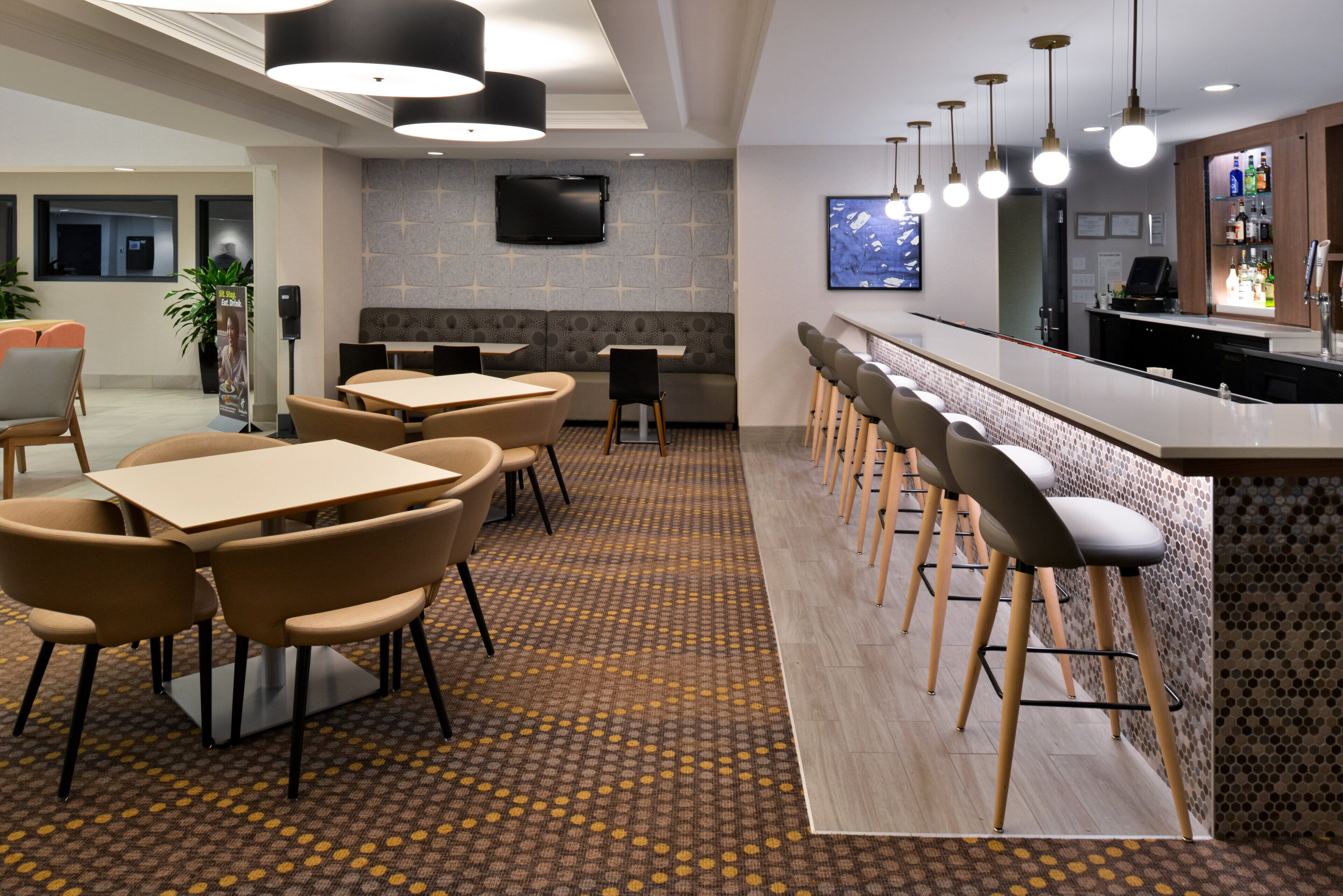 A modern hotel lobby with a bar area, seating arrangements, and a patterned carpet.