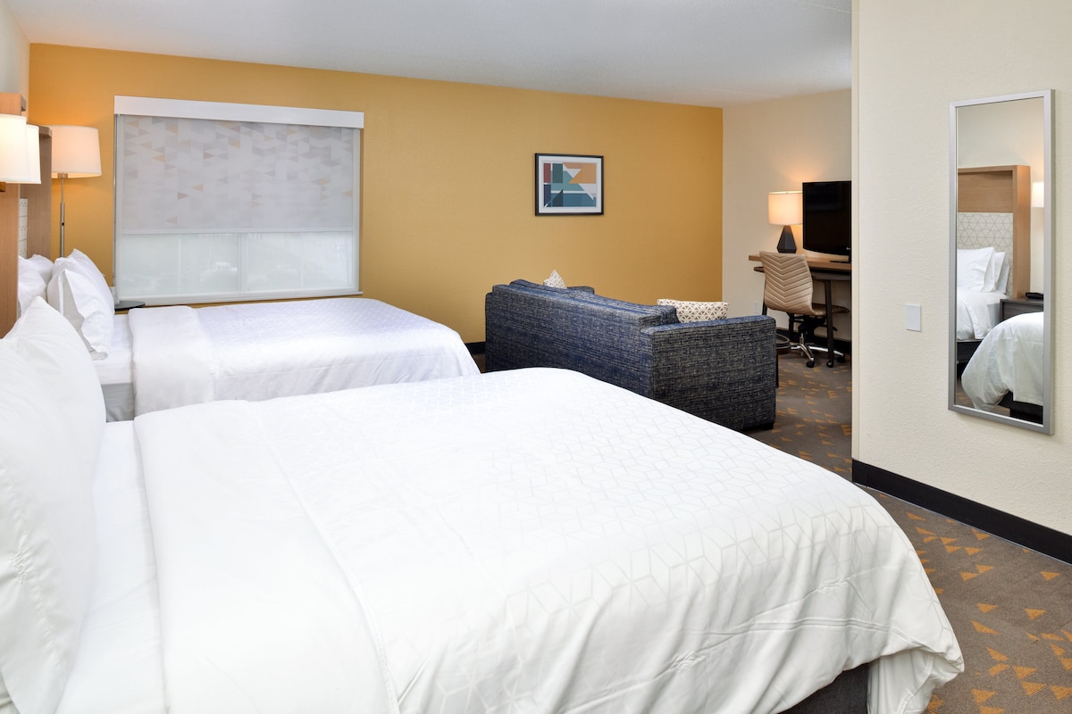 Een hotelkamer met twee bedden, een bank, een bureau met stoel, een televisie en een grote spiegel.