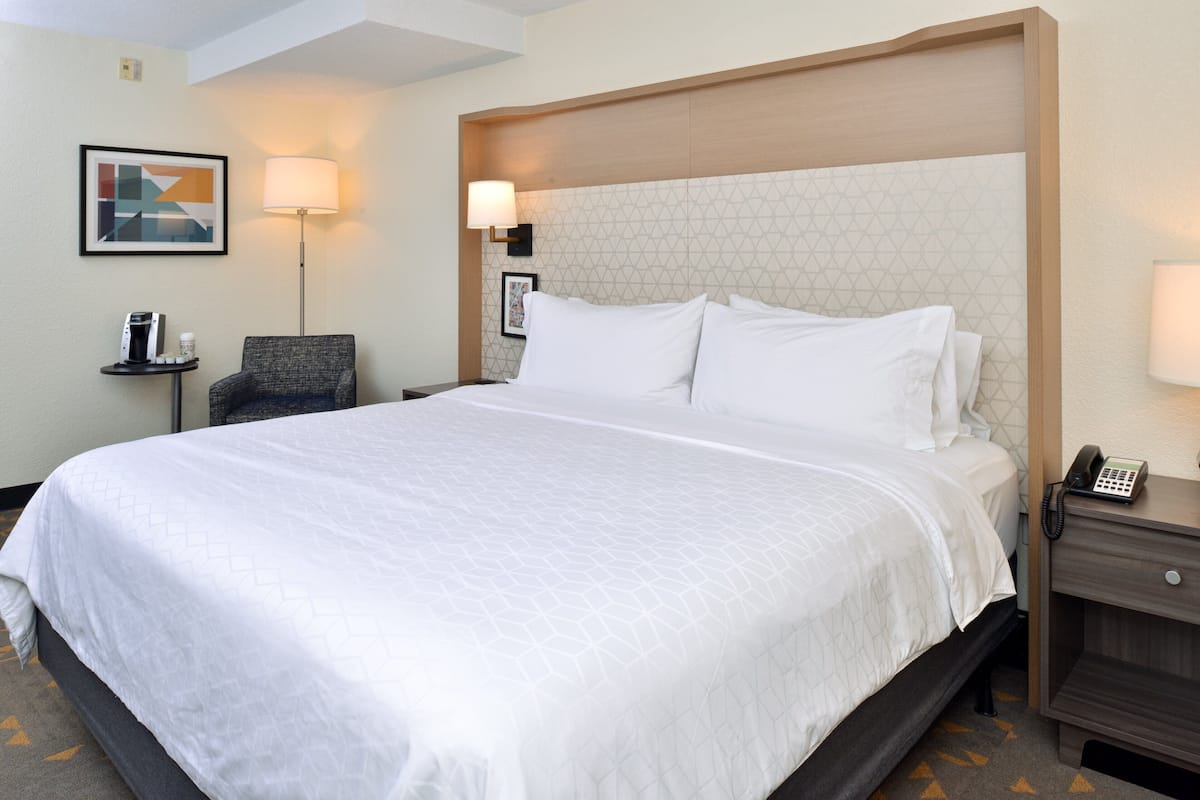 Une chambre d’hôtel avec un grand lit, une chaise, une table de chevet avec un téléphone et une lampe fixée au mur.