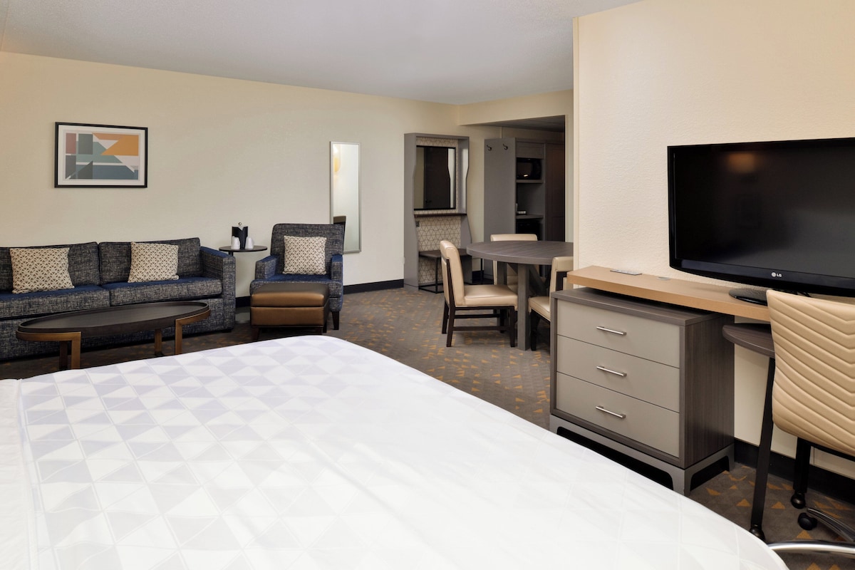 Habitación de hotel con cama, sofá, escritorio con televisor y zona de comedor.