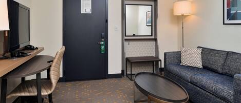 A hotel room with a desk, chair, sofa, and a small table.