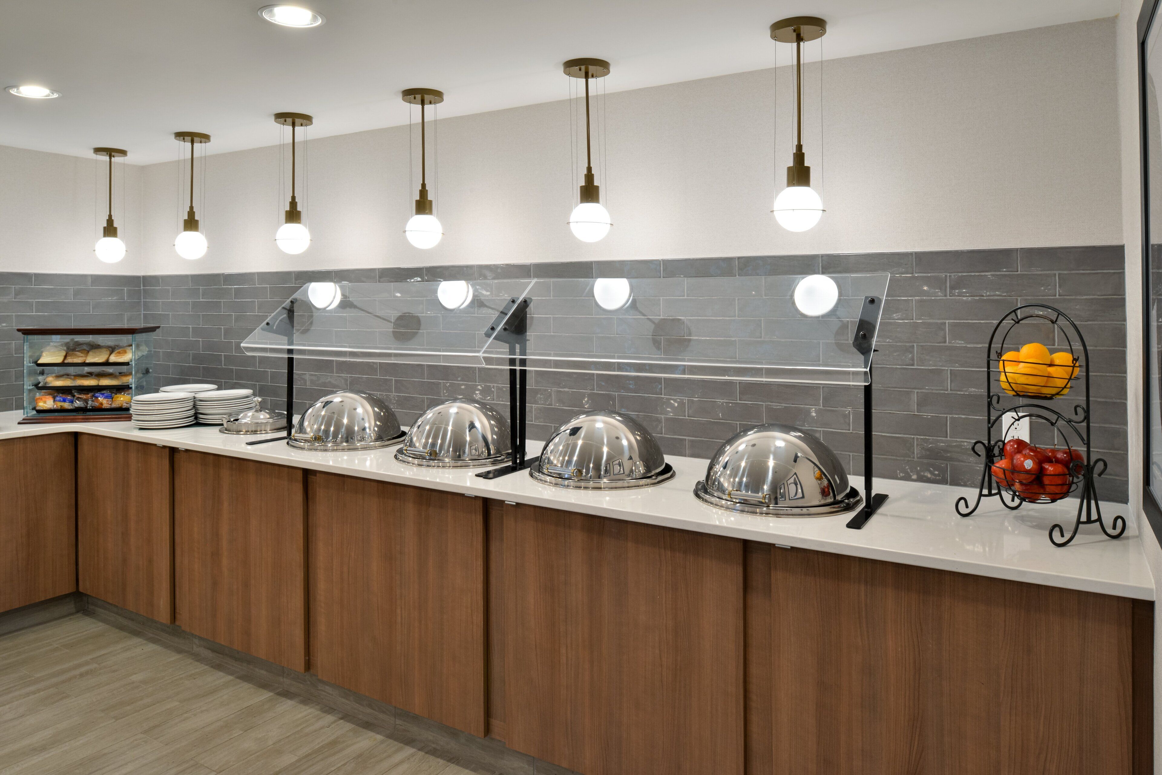 A buffet setup with multiple serving stations, a tiled backsplash, and pendant lighting.