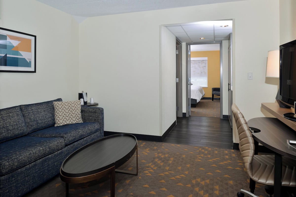 Une chambre d’hôtel avec un canapé bleu, une petite table basse, un téléviseur et un bureau avec une lampe.
