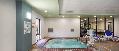 An indoor swimming pool with a lifeguard sign, lounge chairs, and a ceiling with recessed lighting.