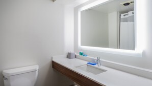 A modern bathroom with a white toilet, a wooden vanity, a large mirror, and a built-in sink. - Holiday Inn Express Hotel & Suites Louisville East by IHG (Louisville)