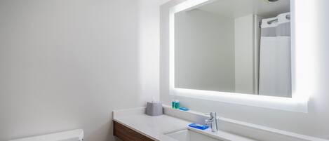 Et moderne badeværelse med et hvidt toilet, en trækommode, et stort spejl og en indbygget vask.