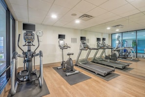 Un gimnasio con equipo cardiovascular, incluyendo cintas de correr y una elíptica, con un espejo grande que refleja el espacio.