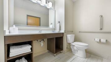 A modern bathroom with a large mirror, white sink, and toilet. There are towels and toiletries on the counter.