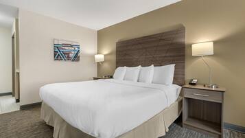 A hotel room with a large bed, a nightstand with a lamp, a small table, and a wall-mounted phone.