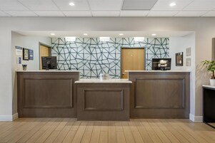 Un área de recepción con dos mostradores, un muro con diseño geométrico y una puerta de madera.