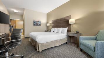 A hotel room with a bed, a desk, a chair, a nightstand, and a lamp.