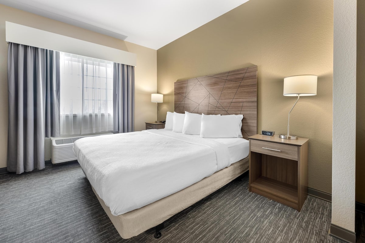 Een hotelkamer met een groot bed, een nachtkastje met een lamp, een venster met gordijnen en een nachtkastje.