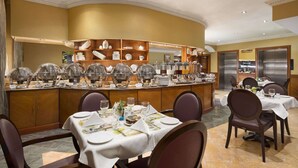 Un buffet avec plusieurs points de service, un îlot central où sont disposés les plats et les boissons, et un espace repas avec des tables et des chaises.