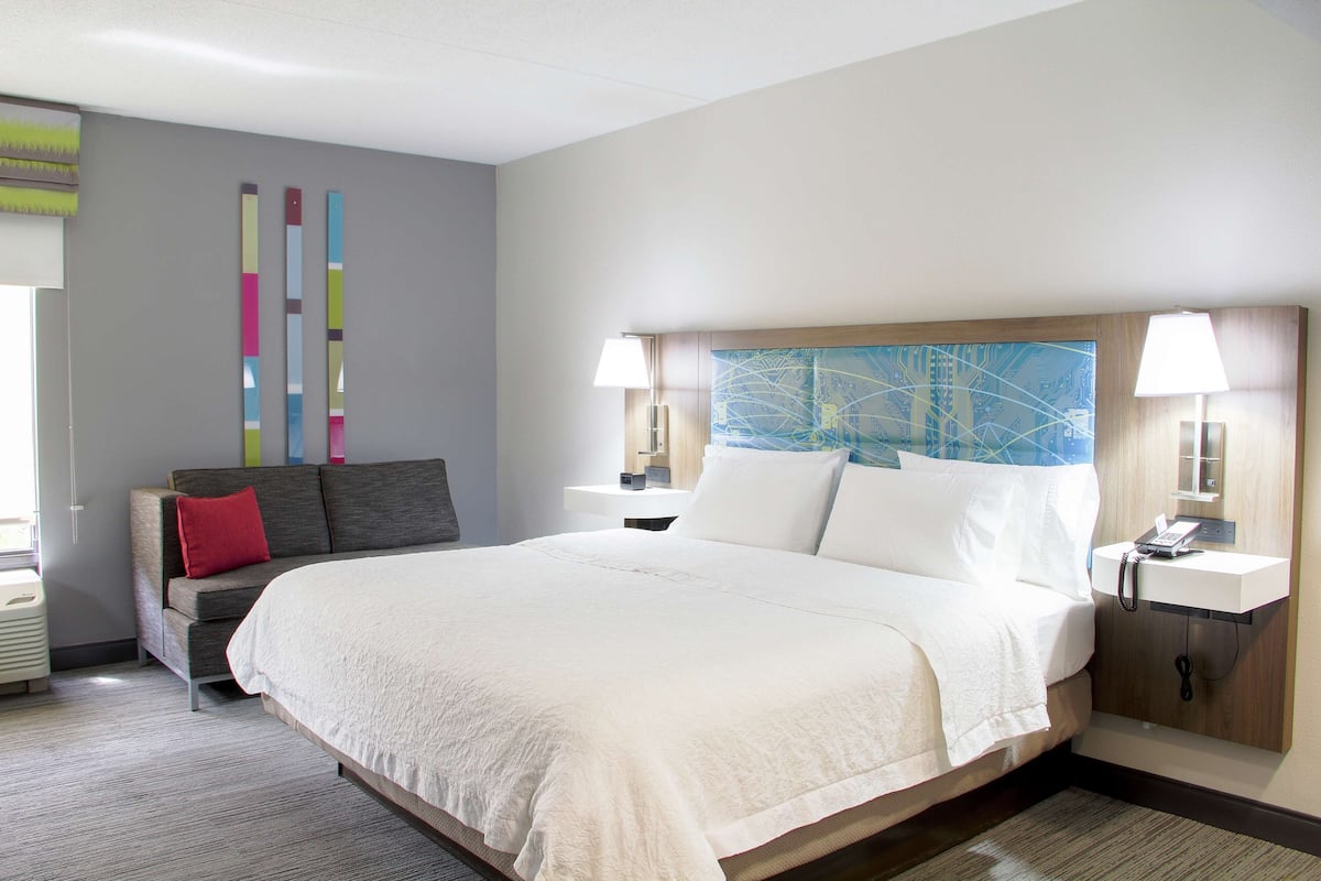 A hotel room with a large bed, a sofa, a desk, and a wall with colorful vertical stripes.