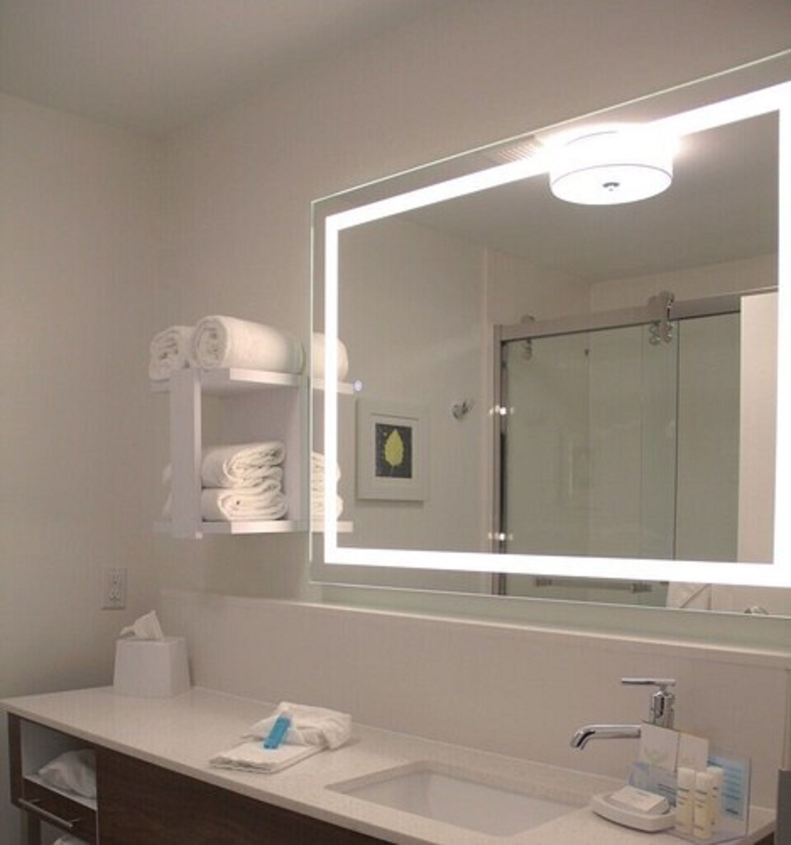 Ett modernt badrum med en stor spegel, en vit tvättställ och en handduksställare med prydligt hopvikta handdukar.