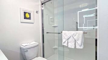 A modern bathroom with a toilet, a glass shower enclosure, and a framed picture on the wall.