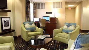 Ein Hotelzimmer mit zwei grünen Sesseln, einem Couchtisch, einem Schreibtisch mit Computer und einem gerahmten Bild an der Wand.