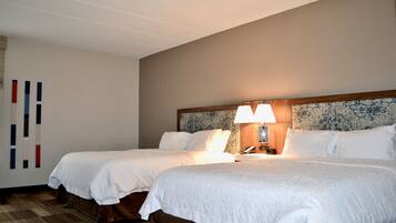 A hotel room with two beds, a headboard with a floral pattern, a bedside table with a lamp, and a wall with vertical stripes.
